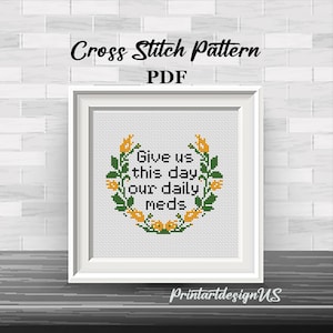 Pode incluir: Um padrão de ponto cruz emoldurado com o texto "Give us this day our daily meds" rodeado por uma coroa de flores. As palavras "Cross Stitch Pattern PDF" e o nome do vendedor também são visíveis.