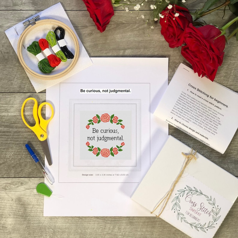 May include: A cross-stitch starter kit with a wooden hoop, embroidery floss, scissors, and a needle threader. The kit includes a pattern with the text "Be curious, not judgmental" surrounded by a floral wreath. The design size is 7.62 x 8.53 cm.