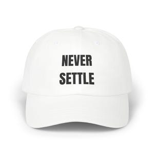 Op de afbeelding: Witte baseballcap met de tekst "NEVER SETTLE" in zwarte letters. De cap heeft een gebogen klep en een ronde kroon. Een casual accessoire.