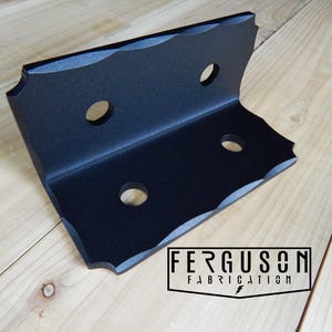 May include: A matte black L-shaped metal bracket featuring a scalloped edge design along the top and bottom. The bracket includes four circular mounting holes and a logo in the corner that reads FERGUSON FABRICATION with a small lightning bolt icon.