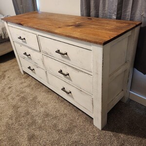May include: White dresser with six drawers and a wood top. The drawers have black metal pulls.