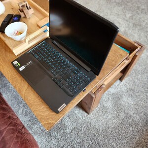 May include: A black laptop computer with a blue backlit keyboard is open on a wooden table. The laptop is on a wooden table with a tray on the left side of the table.