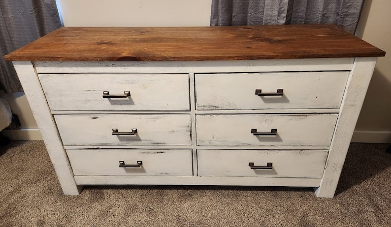 May include: White dresser with six drawers and a wood top. The drawers have black metal handles.