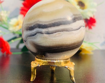 May include: A white and black banded agate sphere on a gold metal stand. The sphere is polished and has a smooth surface.