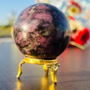 May include: A polished purple and black sphere on a gold metal stand with three legs. The sphere is a crystal ball.