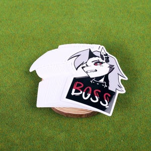May include: A stack of white stickers featuring a black and white illustration of a wolf-like character with red eyes. The character is wearing a black jacket and has the word "BOSS" written in white on a red and black background.