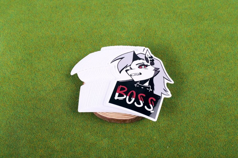 May include: A stack of white stickers featuring a black and white illustration of a wolf-like character with red eyes. The character is wearing a black jacket and has the word "BOSS" written in white on a red and black background.