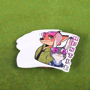 May include: A white sticker with a cartoon image of a fox and a rabbit wearing sunglasses. The text "HUSTLE" is written vertically on the right side of the sticker.