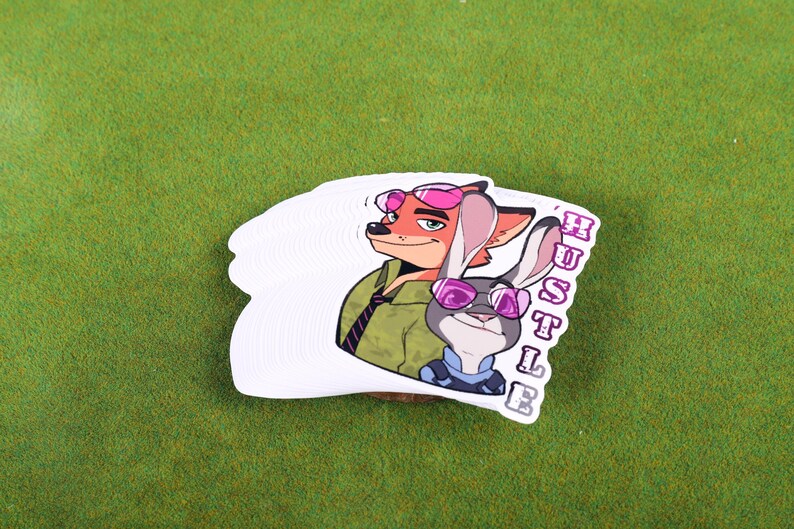 May include: A white sticker with a cartoon image of a fox and a rabbit wearing sunglasses. The text "HUSTLE" is written vertically on the right side of the sticker.
