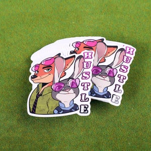 May include: Two stickers featuring cartoon characters from the movie Zootopia. The characters are a fox and a rabbit wearing pink sunglasses. The word "Hustle" is written vertically on each sticker.