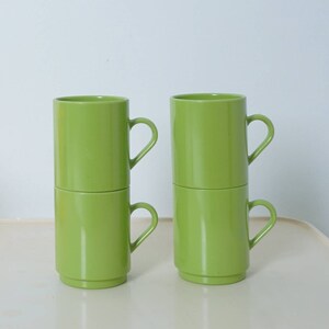 May include: Two sets of stacked green ceramic mugs with handles. Each set has two mugs.