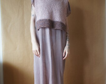 May include: A woman wearing a light pink crocheted sleeveless top over a long, light purple dress. She is wearing brown boots and has brown hair.
