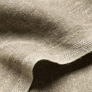 May include: Close-up of a textured, beige linen fabric. The weave is visible, with a slightly irregular pattern. The fabric is folded, creating shadows and highlighting the texture. The color is a neutral, earthy tone.
