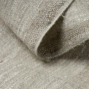 May include: Close-up of a roll of natural-colored linen fabric. The fabric has a coarse, woven texture with visible fibers and a slightly uneven surface. The edges of the fabric are visible, showing the thickness and weave.