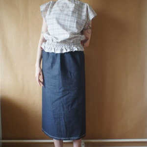 Pode incluir: Uma mulher vestindo uma blusa branca e rosa xadrez com uma bainha franjada e uma saia jeans azul escura. Ela est&aacute; usando sapatos pretos de salto alto.