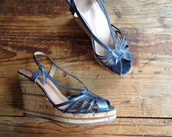 Könnte beinhalten: Ein Paar blaue Ledersandalen mit Keilabsatz und Korksohlen. Die Sandalen haben ein Kreuzriemen-Design und eine offene Zehenpartie.
