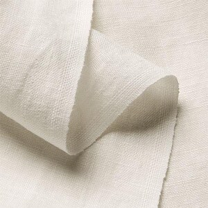 May include: Close-up of a folded piece of off-white linen fabric. The fabric has a textured weave, with visible threads and a slightly rough surface. The folds create shadows and depth, highlighting the material's texture.