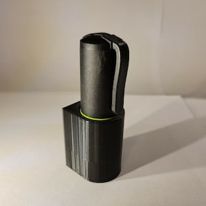 May include: A black 3D printed pen holder with a green accent. The holder is designed to hold a pen with a clip.