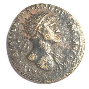Puede incluir: Una moneda romana de bronce con un retrato de un emperador coronado en un lado. La moneda está desgastada y tiene una pátina oscura.