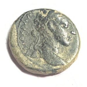 May include: A silver Roman coin with a portrait of a person on one side. The coin has a worn surface and is slightly tarnished.