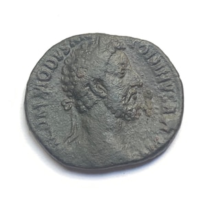 Puede incluir: Una moneda romana de bronce con un retrato de un hombre barbudo con una corona de laurel en la cabeza. La moneda tiene la inscripción "IMP CAESAR AVG F COS III" alrededor del borde.