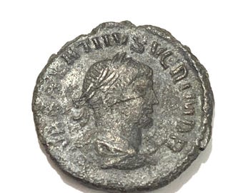 May include: A silver Roman coin with the inscription "IMP. TITVS. S.V.C.N. IMP." around the edge and a portrait of a man with a laurel wreath on his head.