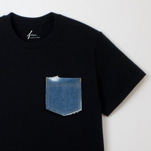 May include: A black t-shirt with a blue denim pocket. The pocket has frayed edges and is slightly distressed.