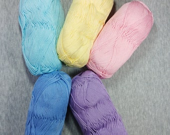 May include: Five balls of yarn in different pastel colors: light blue, yellow, pink, blue, and purple. The yarn is arranged in a star shape on a gray background.