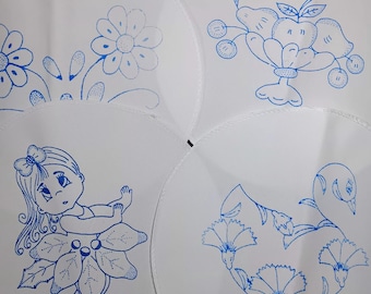 May include: Four white, circular placemats with blue embroidered designs. One features a floral pattern, another a fruit arrangement, a third a girl in a flower dress, and the last a swan with flowers. The designs are detailed and hand-stitched.