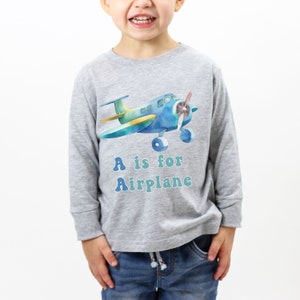 May include: A grey long-sleeved shirt with a blue and yellow airplane graphic and the text "A is for Airplane" in blue and green letters.
