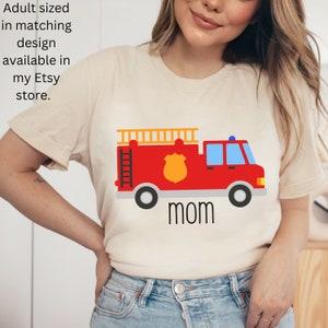 Puede incluir: Una camiseta beige de manga corta con un gr&aacute;fico de un cami&oacute;n de bomberos rojo con una insignia amarilla, una escalera en la parte superior y la palabra mom impresa en negro debajo. El texto Adult sized in matching design available in my Etsy store es visible.