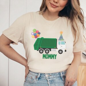 May include: A beige t-shirt with a green garbage truck graphic. The truck has a party hat on top and balloons behind it. The text "Mommy" is printed below the truck.