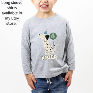 May include: A light gray long-sleeve shirt featuring a cartoon Dalmatian dog wearing a party hat and holding a number 4 balloon. The name "RIVER" is printed below the dog. Text on the left says "Long sleeve shirts available in my Etsy store."