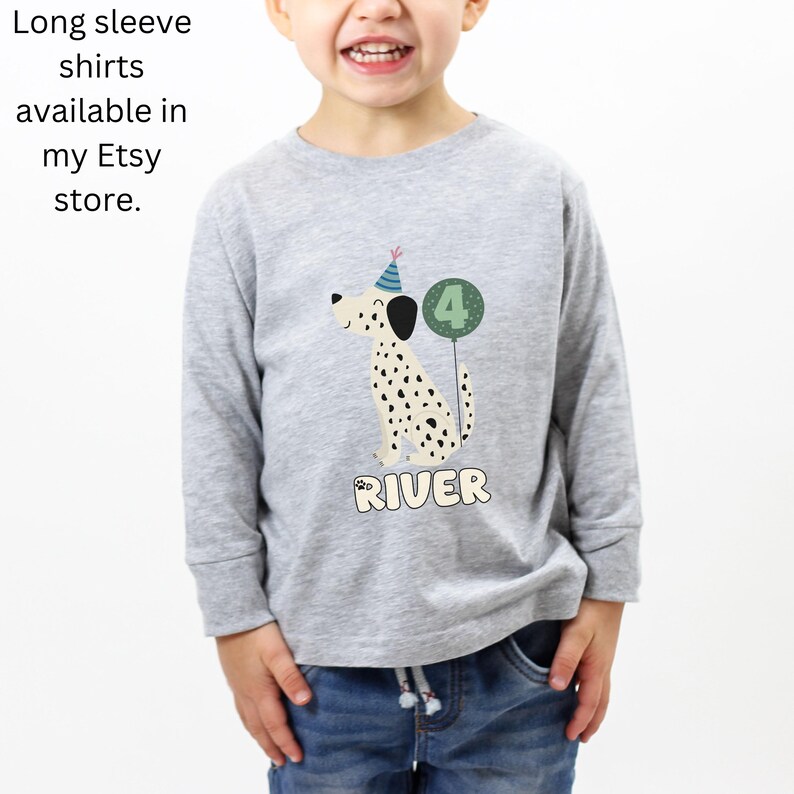 May include: A light gray long-sleeve shirt featuring a cartoon Dalmatian dog wearing a party hat and holding a number 4 balloon. The name "RIVER" is printed below the dog. Text on the left says "Long sleeve shirts available in my Etsy store."