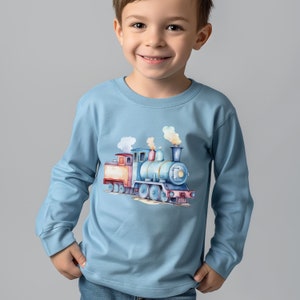 May include: A light blue long-sleeved shirt with a watercolor illustration of a blue, red, and yellow train engine. The train is puffing out smoke and is on a track.