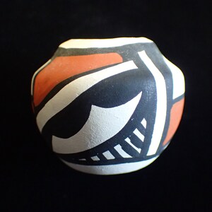 May include: A small, round, black, white, and orange pottery vase with geometric designs.