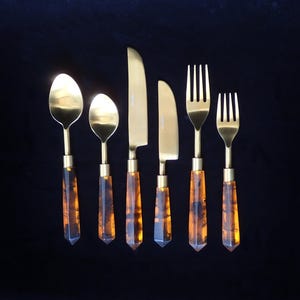 May include: Set of gold-toned cutlery with brown, marbled handles. The set includes two spoons, two forks, and two knives.
