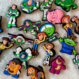 May include: A collection of colourful rubber shoe charms featuring various animated characters including space rangers, a cowboy, a cowgirl, a pink pig, a green alien, a potato-shaped figure, a brown dog, and a purple bear with a cane.