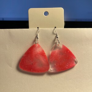 May include: A pair of pink triangle-shaped earrings with silver hooks. The earrings are made of clear resin with pink glitter embedded in the resin.