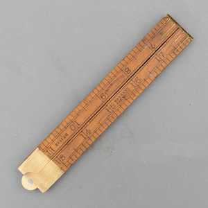 May include: A folding wooden ruler with brass hinges and end caps. The wood is light brown with black printed measurement markings and numbers. Text on the ruler includes "Rabone & Sons Birmingham", "Warranted Boxwood", and "No 1169".