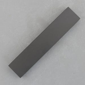 Puede incluir: Un objeto rectangular gris oscuro con un acabado mate. El objeto es largo y estrecho, con un color y textura uniformes. Parece estar hecho de un material sólido, posiblemente metal o un compuesto.