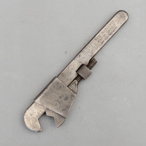 May include: A vintage metal adjustable wrench with a weathered grey finish. The handle features stamped text reading MADE IN ENGLAND, PAT No 389317, and R No 727629. It includes a knurled adjustment nut and a sliding jaw mechanism for gripping.
