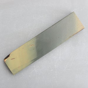 Può includere: Una pietra per affilare rettangolare di colore verde e marrone. La pietra ha una texture ruvida e viene utilizzata per affilare i coltelli.