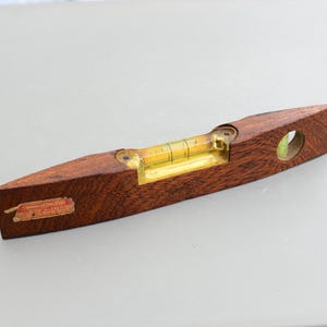 Puede incluir: Un nivel de madera con un nivel de burbuja amarillo y una etiqueta roja que dice "Guaranteed Accurate".