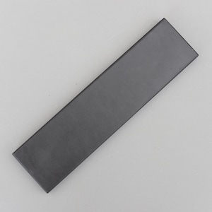 Puede incluir: Un objeto rectangular gris oscuro con un acabado mate. El artículo es un rectángulo largo y estrecho, con un borde ligeramente biselado. El objeto está sobre un fondo gris claro.