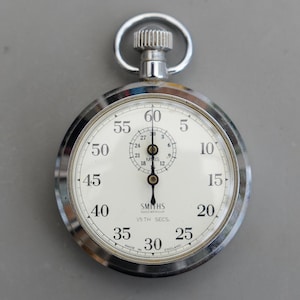 May include: A classic Smiths stopwatch with a silver case and a white dial. The dial features black numerals and markings for seconds and minutes. It has a winding crown and a loop at the top, with 'Made in England' text.