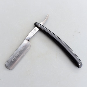 Puede incluir: Una navaja de afeitar recta con mango negro y hoja plateada. La hoja está inscrita con las palabras "HAMBURG PING" y "Made in Germany".