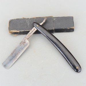 Può includere: Un rasoio da barba vintage con manico in plastica nera e lama argentata. Il rasoio è in una custodia di cartone nero.