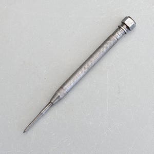 May include: A silver metal centre punch with a textured handle and a pointed tip. The handle is marked "W.T.G. & CO. ENGLAND".