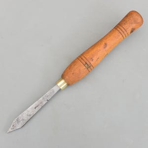 May include: A vintage wood chisel with a brown wooden handle and a metal blade. The handle has three dark bands and a brass ferrule. The blade is slightly worn and has the text "STANLEY" etched on it. The tool is designed for woodworking.